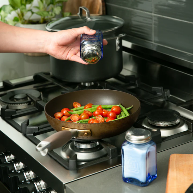 blue glass vintage salt and pepper shakers with salt and pepper inside being used to season cooking veggies in kitchen