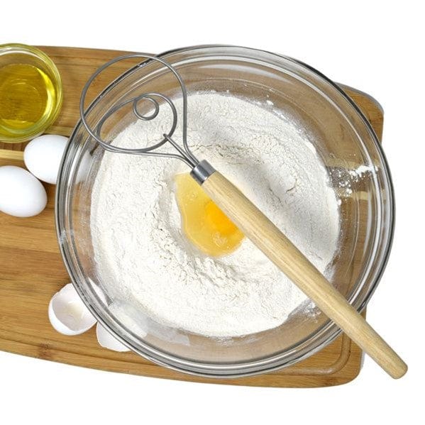 top view of Norpro 12'' Danish Dough Whisk next to two eggs, broken eggshells, a glass cup of oil, and a mixing bowl with egg and dry ingredients for sourdough inside