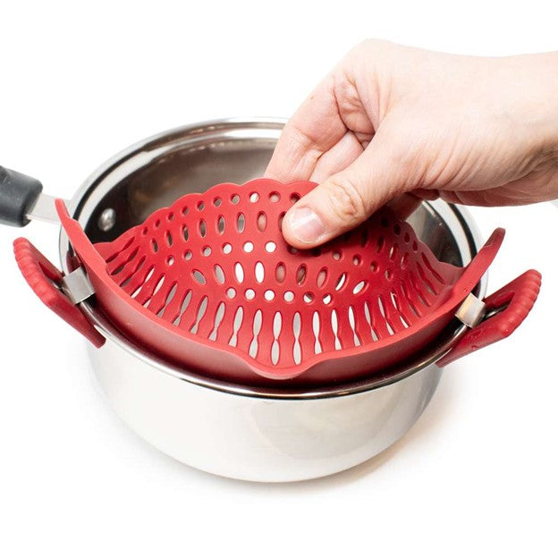 red silicone food strainer attached to silver stainless pot with hand gripping strainer