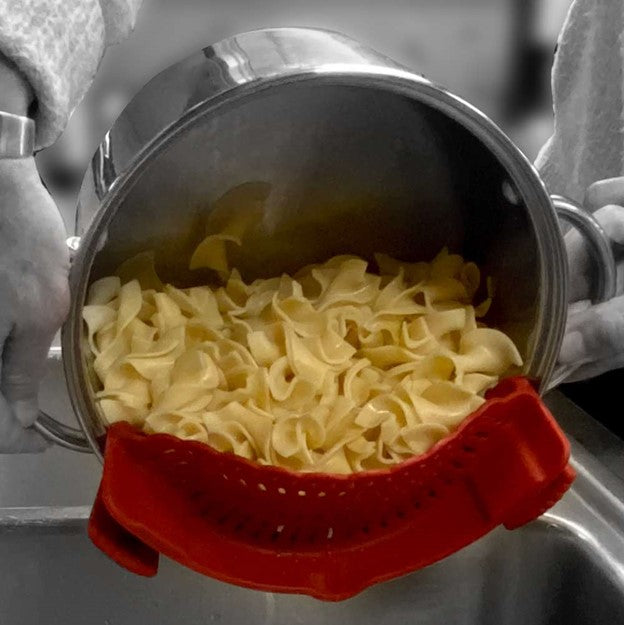 red silicone pasta strainer attached to silver pot draining cooked pasta