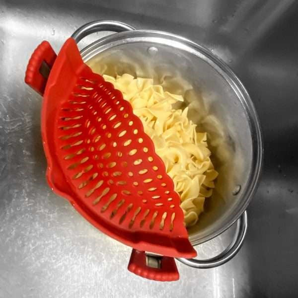 top view of red silicone pot strainer attached to pot with cooked pasta