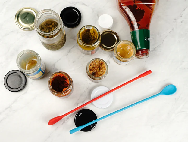 top view of blue and red stirring spoons on kitchen counter next to jars of spices, salad dressings, and condiments