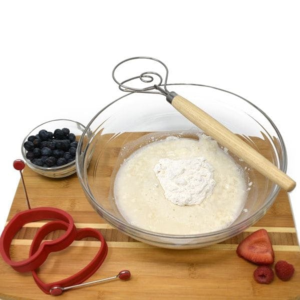 Norpro 12'' Danish Dough Whisk sitting on top of glass bowl with wet and dry ingredients for sourdough muffins and cup of blueberries and raspberries and strawberries next to it, all sitting on bread board